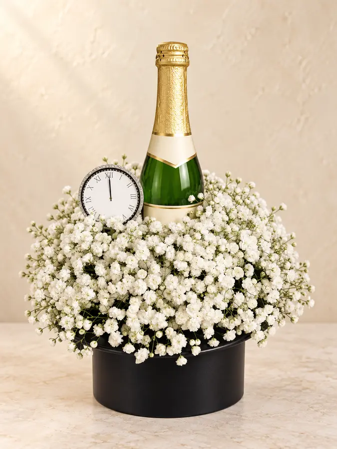 Festliches Geschenkarrangement mit Schleierkraut, Sektflasche und Uhr auf Mitternacht