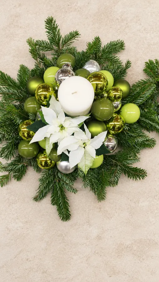 Weihnachtsgesteck aus Tannengrün mit weißem Weihnachtsstern und Kugeln in Grün, Gold und Silber