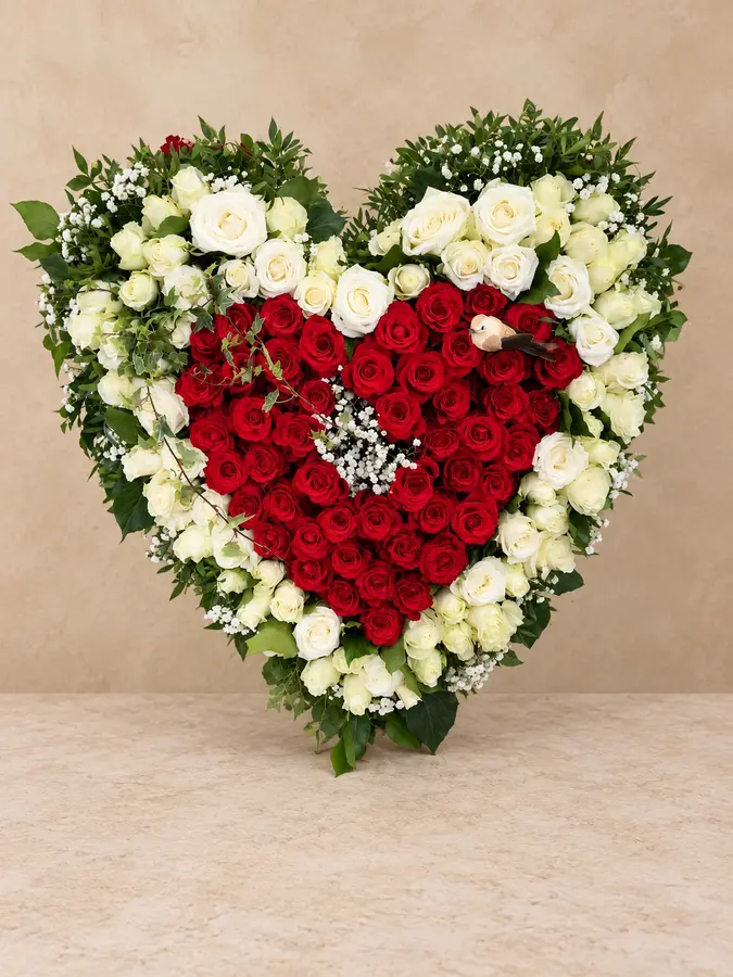 Herzförmiges Trauergesteck aus roten und weißen Rosen mit kleinem Vogel