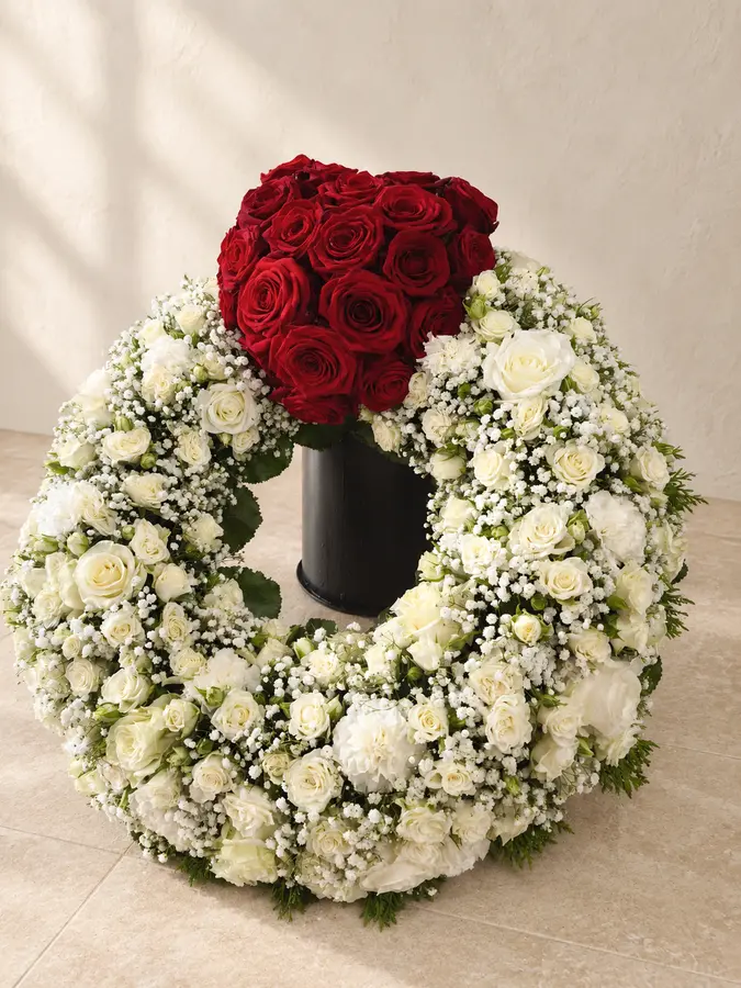 Weißer Trauerkranz mit einer Kugel aus roten Rosen